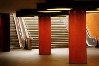 The steps and a disused escalator of a tunnel exit with orange tiles and columns