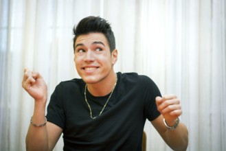 Handsome young man pulling a funny face, indoor shot in front of light white curtains