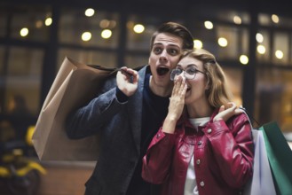 Beautiful couple with shopping bags is talking and smiling while doing shopping in the mall focus