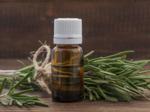 Rosemary essential oil in dark glass bottle and fresh rosemary on dark wooden background with copy