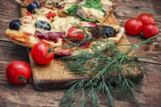 Hunk of delicious meat pizza with bacon and olives on the background of the vegetables.The image is