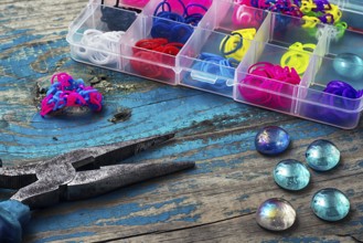 Beads, pliers, and other needlework accessories on outdated turquoise wooden background