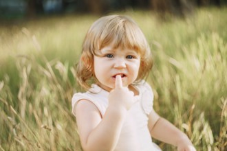 Little girl sits outdoors and holds a finger in his mouth.
