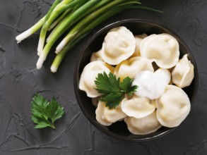 Traditional russian pelmeni, ravioli, dumplings with meat on black concrete background. Top view or
