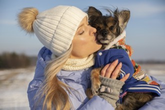 Close-up of a blonde woman hugging her dog. The woman and dog are outside on a winter day. Both are