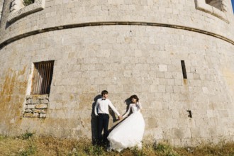 Bride and groom are holding hands and standing tjgether near the wall of the Arza fortress.