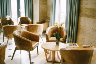 A large hall with exits to the balcony with round tables and flowers and brown armchairs made of