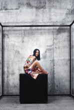 Woman wearing colorful traditional Asian patchwork robe and sitting on a large cube