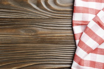 Red checkered napkin on brown wooden kitchen table with copy-space. Top view