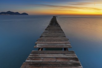 Peaceful sunrise seascape with an old wooden dock leading out into the calm ocean waters of Alcudia
