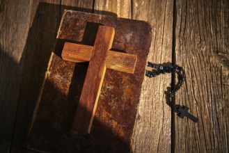 Christian cross on wood bible and rosary beads over wooden vintage background