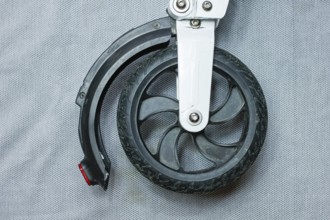 Front wheel and tire of a scooter with a black tire and metal attachment on a grey backdrop
