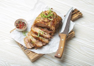 Rolled turkey roasted with spices and herbs on baking paper with knife and wooden white background