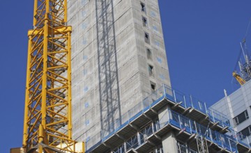 Close up of a large urban construction site with a yellow tower crane casting a shadow on a large