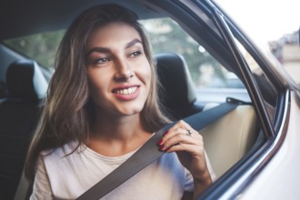 Beautiful woman with phone smiling while sitting on the back seat in the car