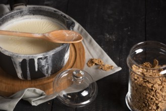 Whole grain cereals in a glass jar with lid and milk in a saucepan, spilled over the edges, on a