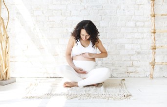 Beautiful brunette pregnant woman stretching and practicing yoga at home