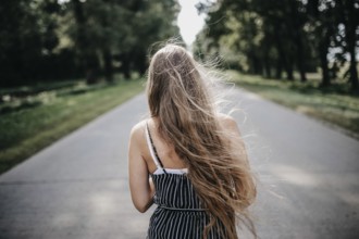 Woman with long hair walks on a road surrounded by lush greenery
