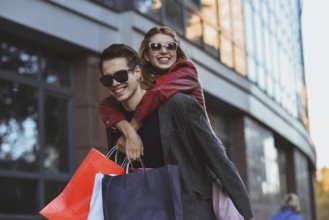 Happy couple shopping together and having fun. Boyfriend carrying his girlfriend on the piggyback