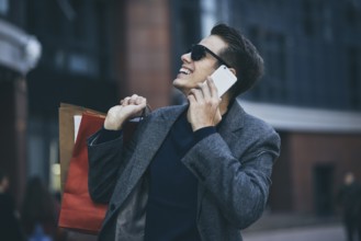 Positive cool guy with sunglasses and paper bags walking near showcase with reflection