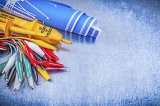 Yellow electrical tester crocodile cables set blue construction plans on metallic background