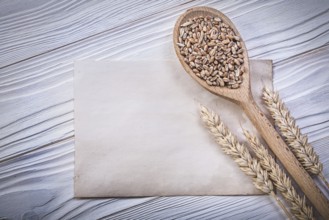 Ripe wheat rye ears grain wooden spoon clean vintage paper sheet on wood board top view