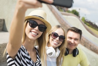 Three young happy people sitting outdoors and making selfie