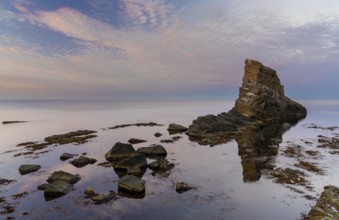 Colorful sunset over the Black Sea coast of Bulgaria with a sea stack and rocks in the calm water