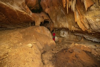 A speleologist with helmet and headlamp exploring a cave with rich stalactite and stalagmite