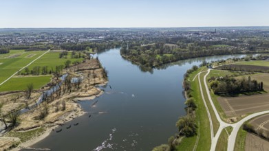 View of a river (Danube) with riverside vegetation, neighbouring fields and a town in the distance,