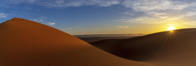 A panorama view of the sand dunes at Erg Chebbi in Morocco at sunset with a sunstar