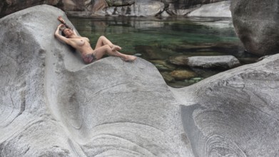 A woman lying in a comfortable position on a smooth granite rock on the bank of a river, Verzasca