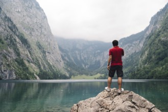 Man standing on rock looking at beautiful and misty lake in the alps. Obersee