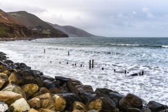 Scenic view of rocky beach in the coast of Ireland against mountains and cloudy sky
