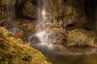 Closeup view of a forest waterfall in sunlight with autumn leaves and mossy stones