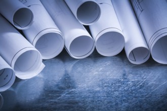 Set of rolled up white construction drawings on scratched silver-metal surface building and