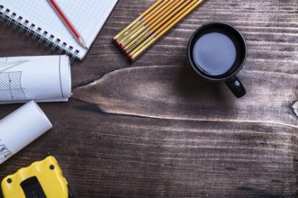 Notepad pencil blueprints tape measure wooden meter and cup of coffee on wood board