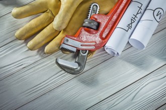 New plumb wrench leather gloves and rolled piping blueprints on vintage wood background