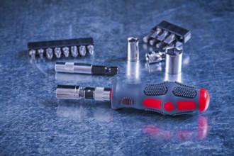 Insulated screwdriver with interchangeable bits and heads on scratched metallic background