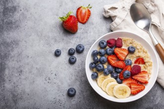 Oatmeal porridge with fruit and berries in bowl with spoon on gray stone background table top view,
