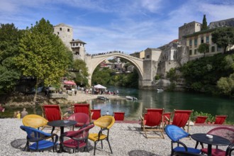 Cafe with colourful chairs on the banks of the river Neretva, behind the bridge Stari Most, old
