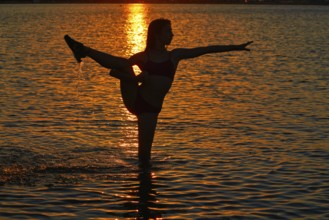 Girl gymnastics pose at sunset beach in orange sky