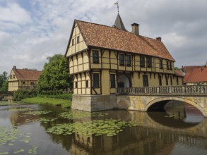 Half-timbered house stands picturesquely on a watercourse with water lilies and a stone bridge,