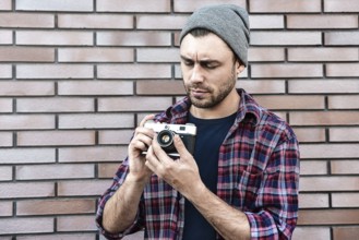 Man with retro photo camera Fashion Travel Lifestyle outdoor while standing against brick wall