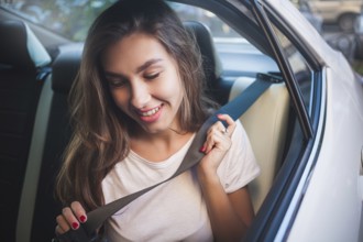 Beautiful woman with phone smiling while sitting on the back seat in the car