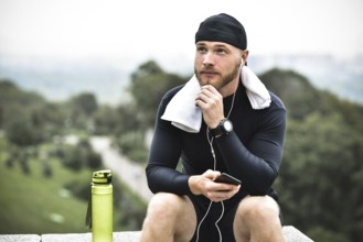 Muscular bearded athlete with towel checking burned calories on smartphone after good workout