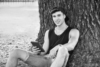 Smiling Young Handsome Man, Reading on Ebook Reader or Holding a Tablet Computer, Relaxing on