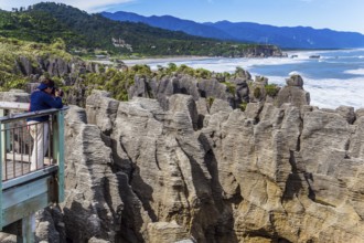 Observation deck. Woman takes pictures of rocks and ocean surf. New Zealand. Stone flat pancakes,