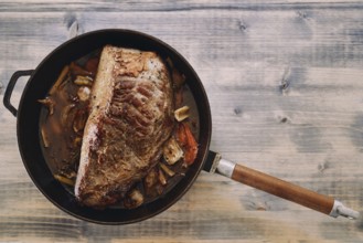 Juicy roast beef with a baked crust in vegetables and sauce stands in a pan on the table.