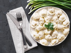 Traditional russian pelmeni, ravioli, dumplings with meat on black concrete background. Top view or